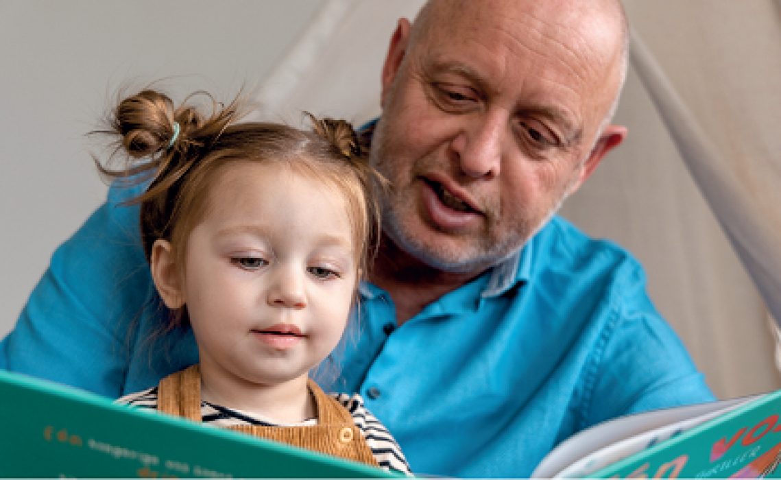Man leest kleuter voor, beide kijken aandachtig naar het boek.