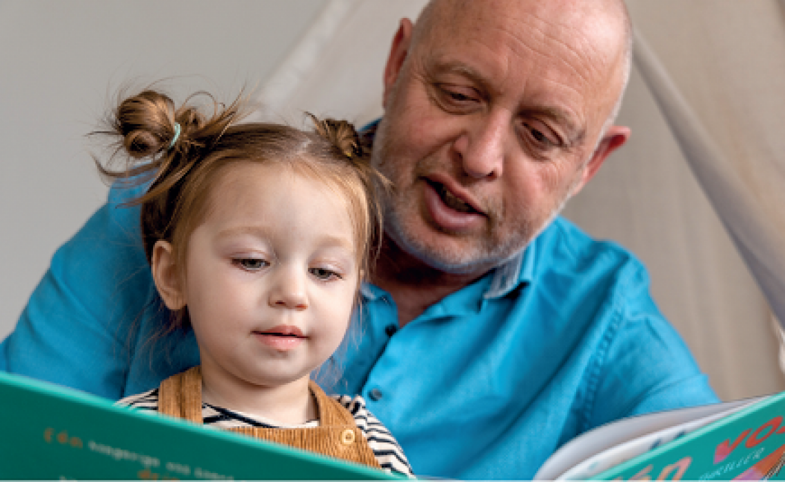 Man leest kleuter voor, beide kijken aandachtig naar het boek. 