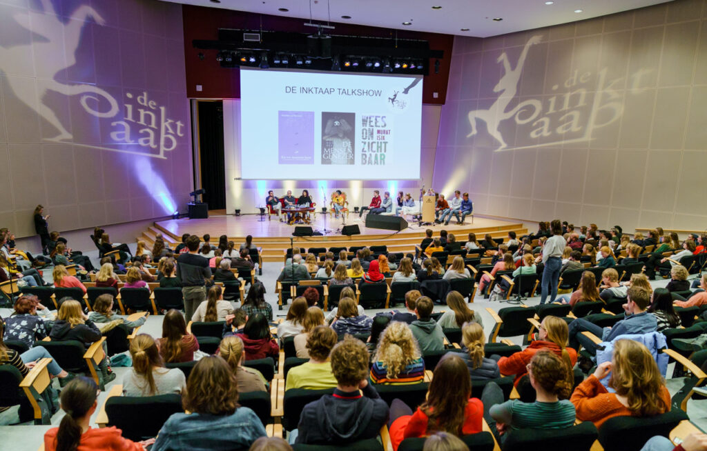 Gevulde zaal, deelnemers kijken naar beamer met daarop de presentatie van De Inktaap.