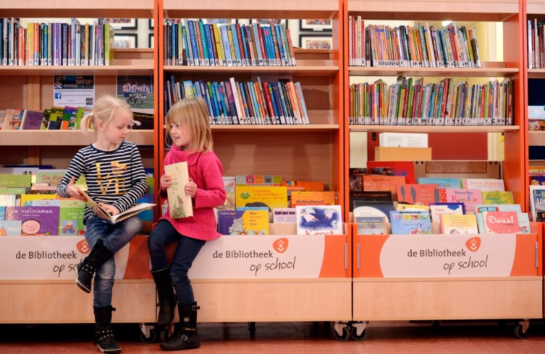 twee meisjes op de rand van de browserbak van een van de kasten van de schoolbibliotheek