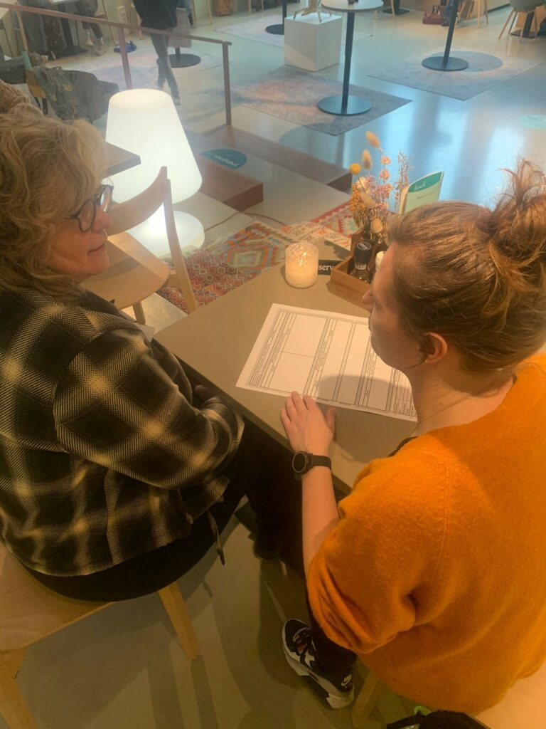 Twee personen aan tafel met een gespreksmodel op papier, om de uitkomsten duidelijk op te schrijven.