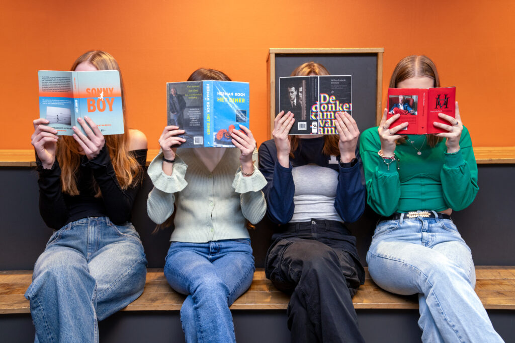 Leerlingen lezen op een rij, met een boek voor hun gezicht