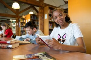 Leerlingen zitten met boek aan tafel in mediatheek