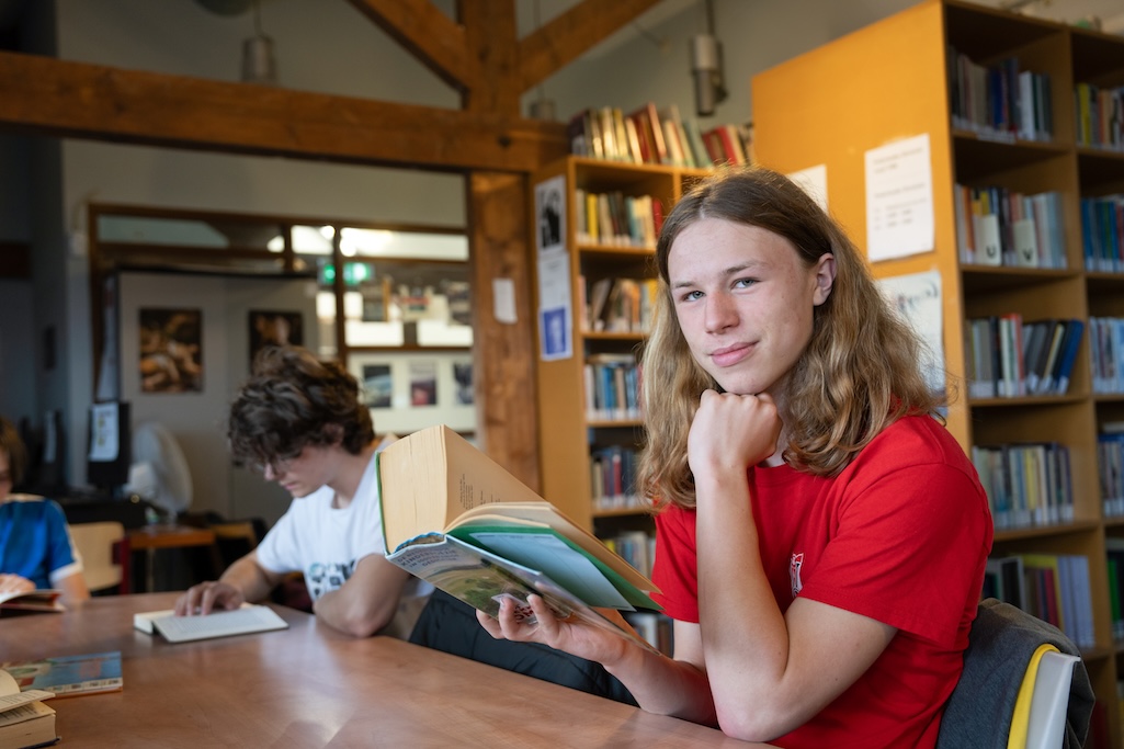Leerling met boek in handen in een mediatheek aan tafel
