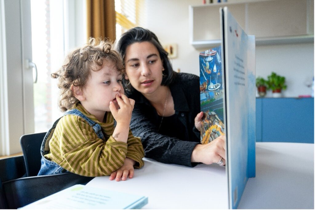Kind wordt voorgelezen uit prentenboek aan de keukentafel