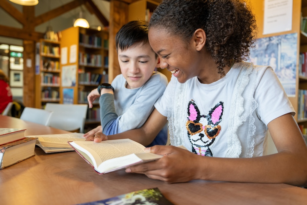 Twee scholieren lezen naast elkaar een boek in de schoolbibliotheek.