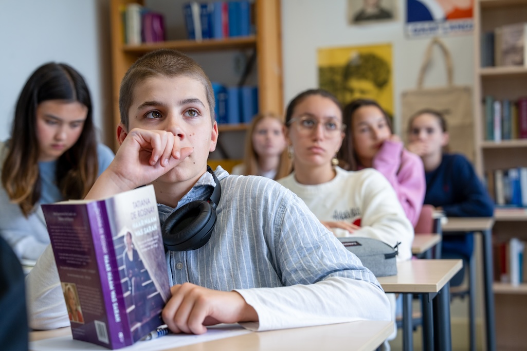 Leerlingen kijken naar voren in de klas, met boek op tafel